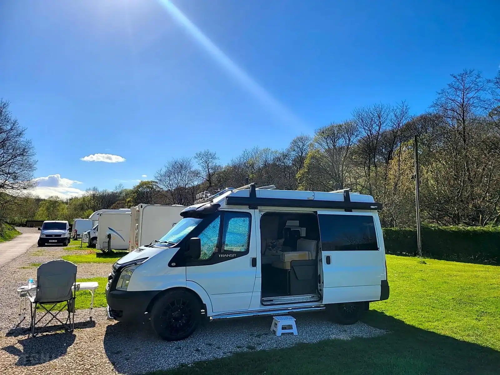 A campervan on a sunny hardstanding pitch at Riverside, with caravans and trees behind